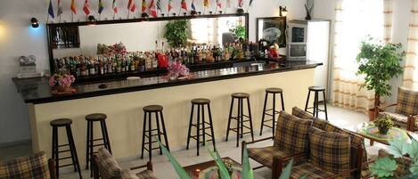 A bar area with stools, a counter with bottles, and a seating area with plaid sofas and chairs.