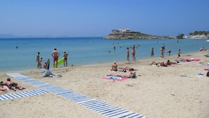 Una playa con gente tomando el sol, nadando y caminando por la orilla.