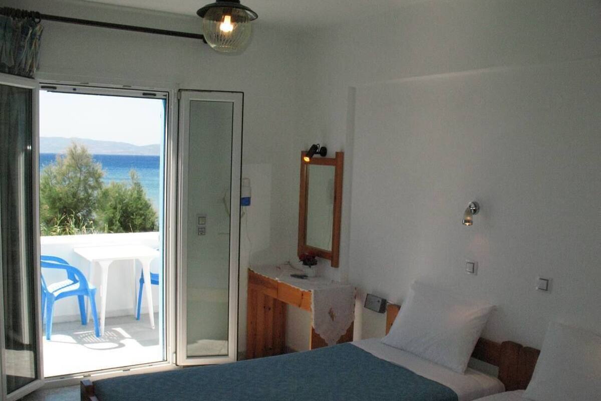 A room with two beds, a desk, a mirror, and a view of the sea.