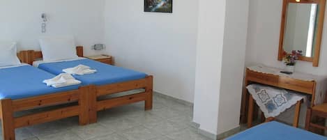A room with two wooden beds, a small desk with a mirror, and a painting on the wall.