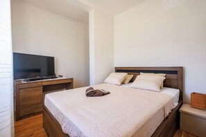 A neatly made bed with a patterned bedspread, a television on a wooden stand, and a wooden nightstand with a small decorative item. - Perfect 3-bedroom house with heated pool in peaceful Šestanovac (Šestanovac)