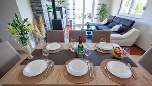 A dining table set with plates, cutlery, and a bottle, surrounded by chairs in a modern living area with a sofa and plants. - Perfect 3-bedroom house with heated pool in peaceful Šestanovac (Šestanovac)