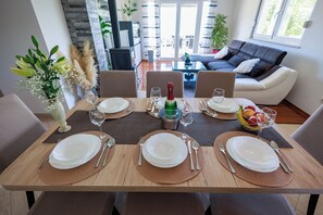 A dining table set with plates, cutlery, and a bottle, surrounded by chairs in a modern living area with a sofa and plants. - Perfect 3-bedroom house with heated pool in peaceful Šestanovac (Šestanovac)