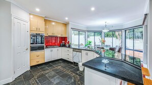 A modern kitchen with a black tiled floor, white and wooden cabinets, a built-in oven, and a large window overlooking a backyard. - StayAU PoolTable 2-Story Pet-friendly  (Caroline Springs)