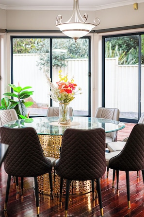 Uma área de refeições com mesa de vidro, cadeiras acolchoadas, um vaso com flores e um candelabro.