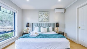 A bedroom with a large bed, two bedside tables, a window, and an air conditioning unit. - StayAU PoolTable 2-Story Pet-friendly  (Caroline Springs)