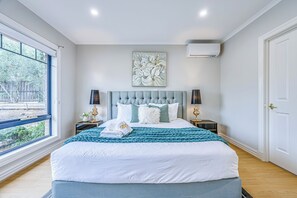 A bedroom with a large bed, two bedside tables, a window, and an air conditioning unit. - StayAU PoolTable 2-Story Pet-friendly  (Caroline Springs)