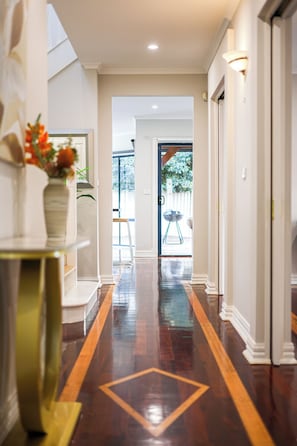 A hallway with a polished wooden floor, white walls, and a door leading outside. - StayAU PoolTable 2-Story Pet-friendly  (Caroline Springs)