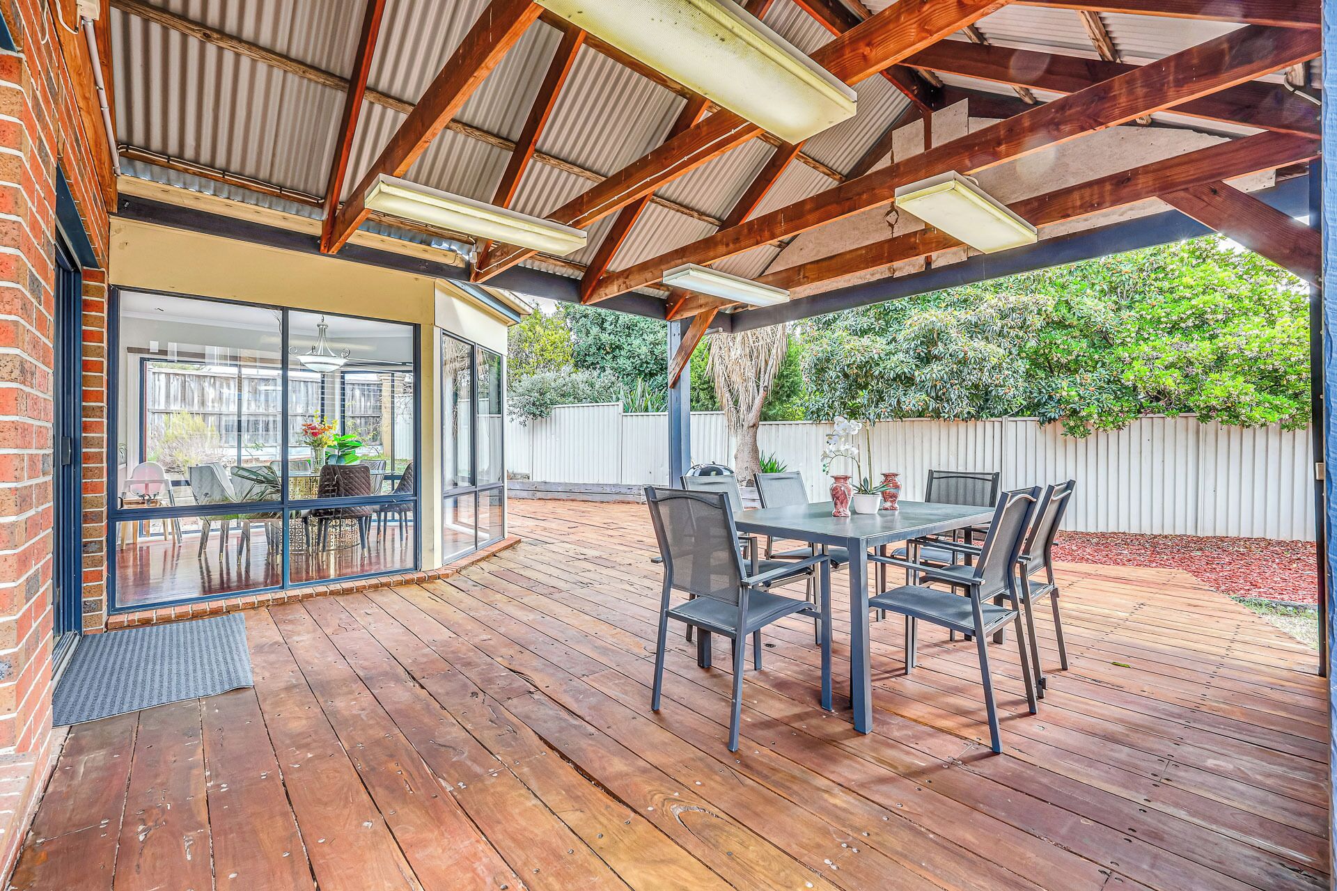 A covered patio with a wooden deck, a table with chairs, and a glass door leading to an indoor area.