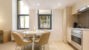 A modern kitchen with a dining area, large windows, and a built-in oven. - Luxuria Apartments - Degraves Place (Melbourne)