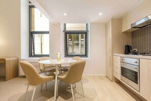 A modern kitchen with a dining area, large windows, and a built-in oven. - Luxuria Apartments - Degraves Place (Melbourne)