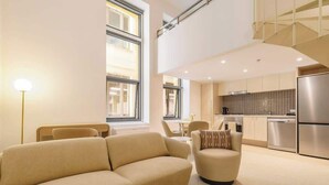 A modern living room with a sofa, armchair, and dining area. - Luxuria Apartments - Degraves Place (Melbourne)