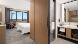 A hotel room with a bed, desk, chair, large windows, and a bathroom with a mirror and sink. - Hampton by Hilton Tianjin Baodi (Tianjin)