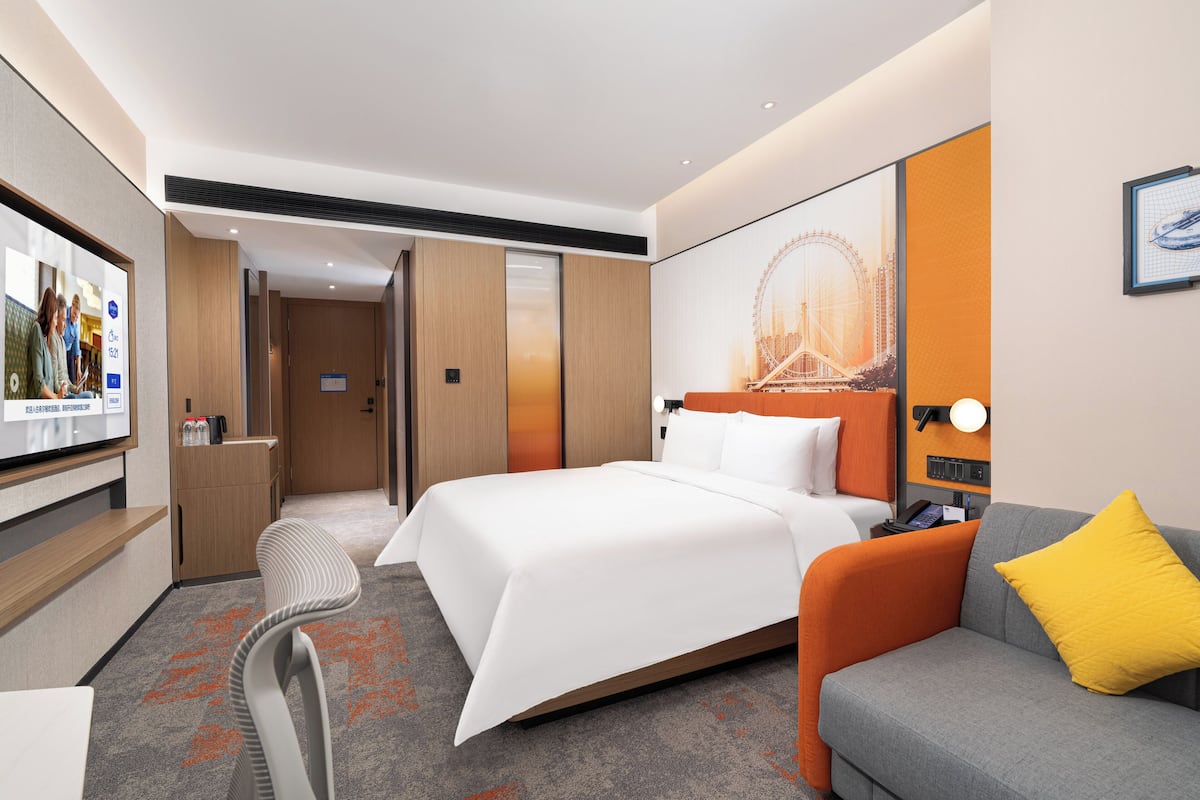 A hotel room with a bed, a sofa, a TV, and a poster of a Ferris wheel.