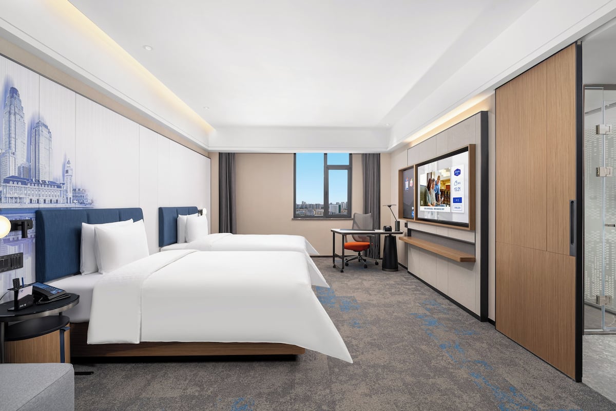 A hotel room with a bed, desk, chair, and a large TV screen.
