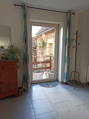 Ein Zimmer mit einem Holzschrank, einem Blumentopf, einem Kleiderständer und Blick auf ein Steinhaus.