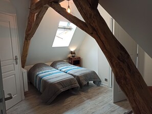 Ein Schlafzimmer mit schrägem Dach, einem Oberlicht, zwei Betten mit gemusterten Betttextilien, einem Nachttisch mit Lampe und einem Holzbalkenbau.