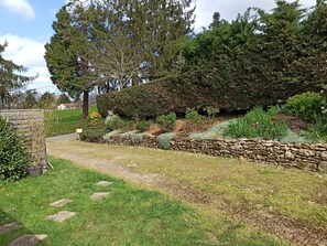 Ein Gartenweg mit Steinmauer, verschiedenen Sträuchern und Bäumen.