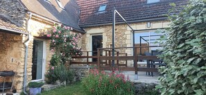 Ein Steinhäuschen mit einer Holzterrasse, einem Metallzaun und einem blühenden Garten.
