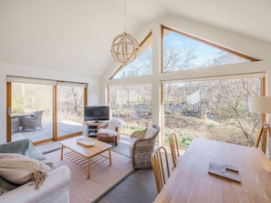 Ein geräumiger Raum mit großem Fenster, Fernseher, Esstisch und einer Couch.