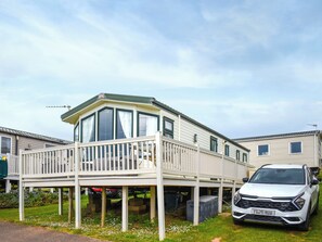 A mobile home with a balcony, a car parked in front, and a grassy yard. - 3 bedroom accommodation in Exmouth (Exmouth)