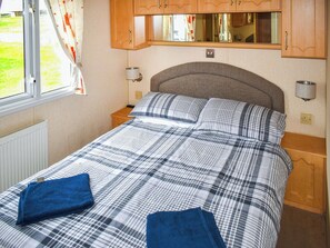 A bedroom with a bed, curtains, wooden cabinets, a mirror, and a window. - 3 bedroom accommodation in Exmouth (Exmouth)