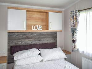 Ein Schlafzimmer mit einem Bett, weißen Kissen, einem Kopfteil mit der Aufschrift 'LOVE' und hängenden Holzschränken über dem Bett. Ein Fenster mit gemusterten Vorhängen ist ebenfalls zu sehen.