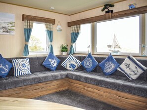 Ein gemütliches Wohnzimmer mit grauem Sofa, verziert mit nautisch inspirierten Kissen, einer Holzvertäfelung und einem Fenster mit Blick auf ein Segelboot.