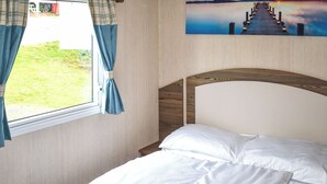 Ein Bett mit weißer Bettwäsche, ein Fenster mit Vorhängen und ein Gemälde eines Piers an der Wand.