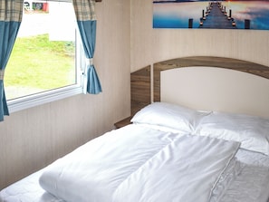Ein Bett mit weißer Bettwäsche, ein Fenster mit Vorhängen und ein Gemälde eines Piers an der Wand.