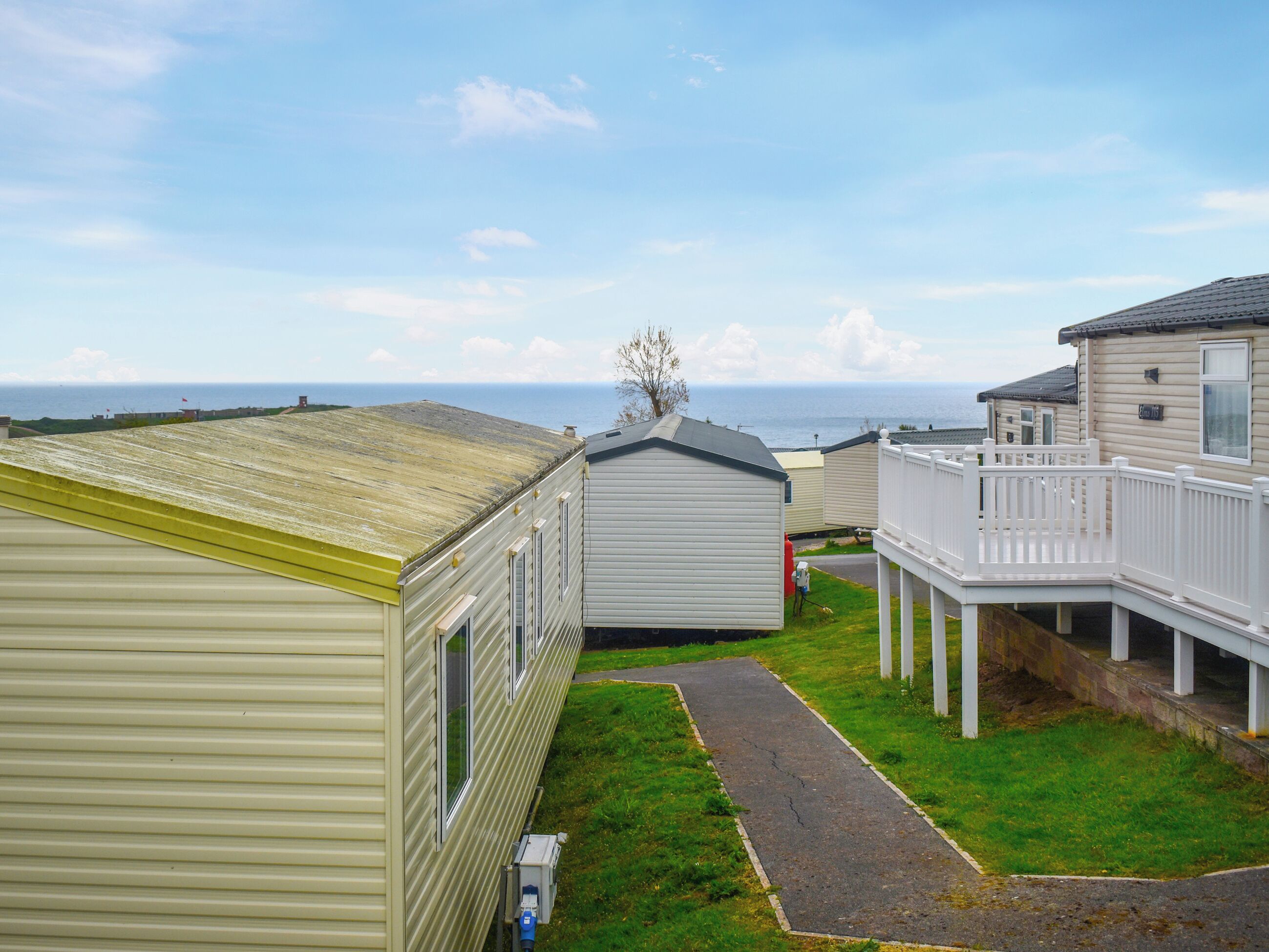 A row of mobile homes with a grassy yard and a pathway leading to a dock.