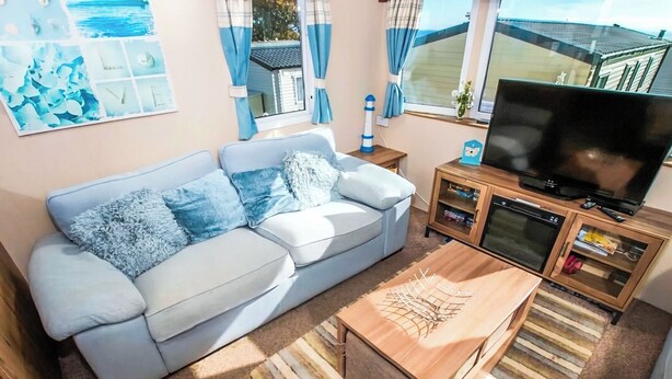 A living room with a sofa, a coffee table, a television, and a cabinet. - 2 bedroom accommodation in Exmouth (Exmouth)