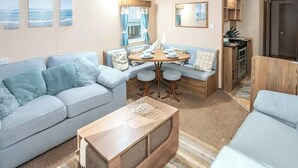 A compact living space with a sofa, a coffee table, a dining table with chairs, a kitchenette, and a window with curtains. - 2 bedroom accommodation in Exmouth (Exmouth)
