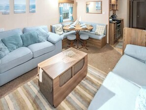 Ein gemütlicher Wohnbereich mit Sofa, Couchtisch, Esstisch mit Stühlen, Küchenzeile und einem Fenster mit Vorhängen.