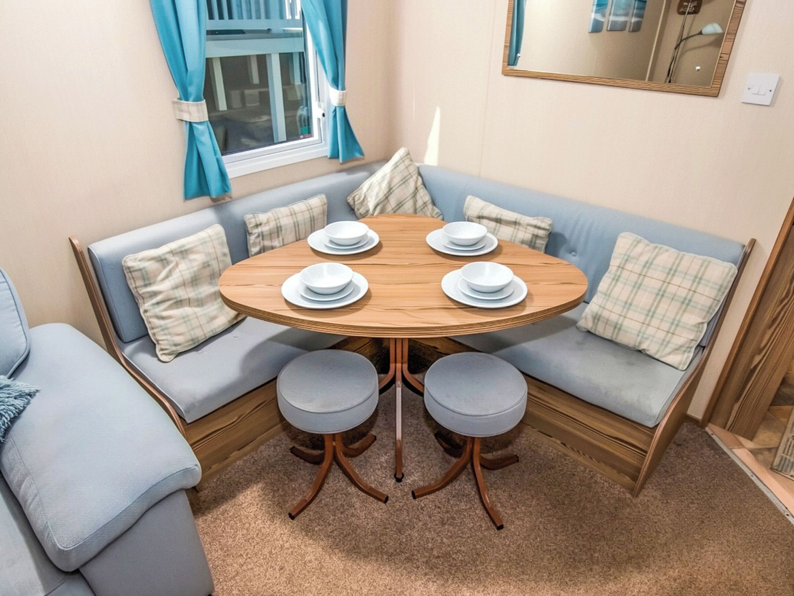 Een gezellige kamer met een ronde houten tafel, twee zachte zithoeken in blauw en een raam met gordijnen.