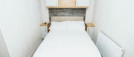 A small, neatly arranged bedroom with a bed, two nightstands, a wooden headboard, and built-in cabinets.