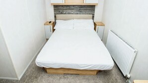 Une petite chambre à coucher, bien rangée, avec un lit, deux tables de chevet, une tête de lit en bois et des placards intégrés.