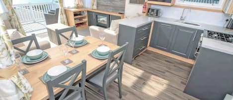 A modern kitchen with grey cabinets, a wooden dining table set for four, and a view of the ocean through large windows.