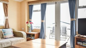 Huoneessa on sohva, puinen pöytä, TV-taso ja ikkuna, jossa on verhot.
