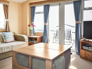 Ein Zimmer mit einer Couch, einem Holztisch, einer TV-Konsole und einem Fenster mit Vorhängen.