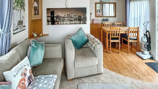 Ein Wohnzimmer mit einer Couch, einem Esstisch mit Stühlen, einer Küchenzeile und einem großen Fenster mit Vorhängen.