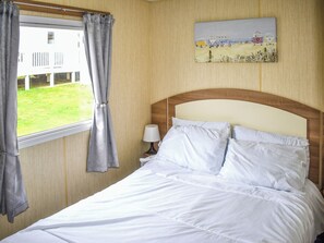 Ein Hotelzimmer mit Bett, einem Vorhangfenster, einer Lampe und einem Bild an der Wand.
