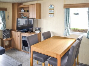 Ein kompaktes Wohnmobil-Interieur mit einem Holztisch, vier Stühlen, einem Fernseher und einem kleinen Regal mit Dekoration.