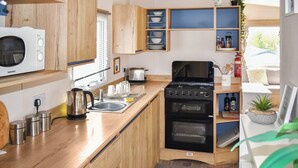 A compact kitchen with wooden cabinets, a built-in oven, a microwave, and a sink. - Juniper Close 52 - UKC9405 (Exmouth)