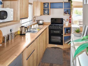 A compact kitchen with wooden cabinets, a built-in oven, a microwave, and a sink. - Juniper Close 52 - UKC9405 (Exmouth)