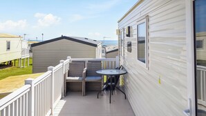 Une terrasse avec une table et des chaises, donnant sur d’autres maisons mobiles, et un mur extérieur blanc.