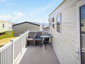 A deck with a table and chairs, a view of other mobile homes, and a white exterior wall. - Karo Place 113 - UKC9404 (Exmouth)