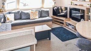Un salon moderne avec un canapé gris, un téléviseur à écran plat, une table basse en bois et une table à manger ronde.