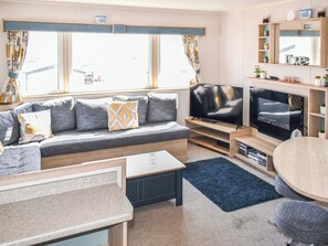 A modern living room with a grey sofa, a flat-screen TV, a wooden coffee table, and a round dining table. - Karo Place 113 - UKC9404 (Exmouth)