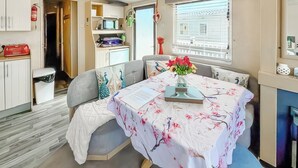 Quarto com mesa de jantar, sofá, janela com persianas e um espaço com cozinha compacta.